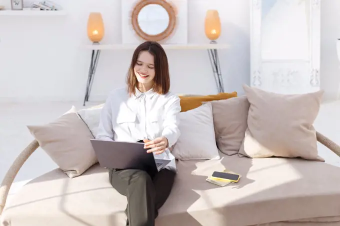 Young smiling woman in business style clothes works in laptop at home