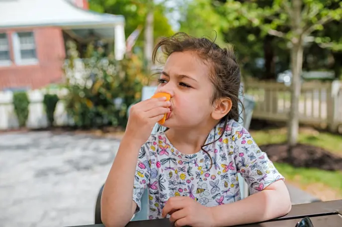 Young girl eating orange slice sitting outside
