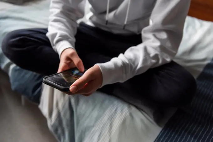 Close up of hands of teen boy in white sweater texting on phone.