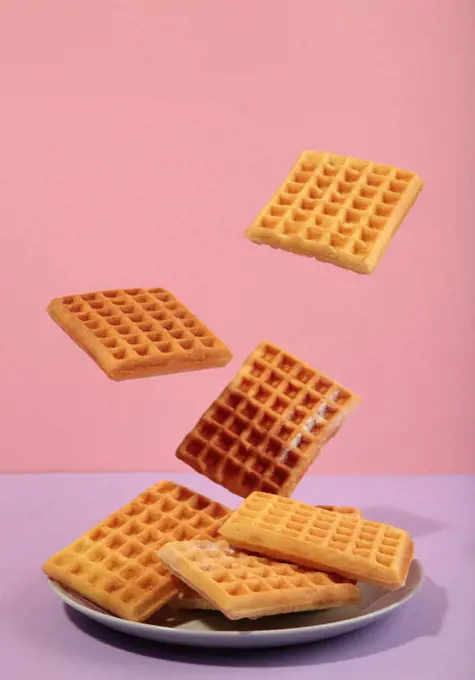 Belgian waffles flying in air on pink background.