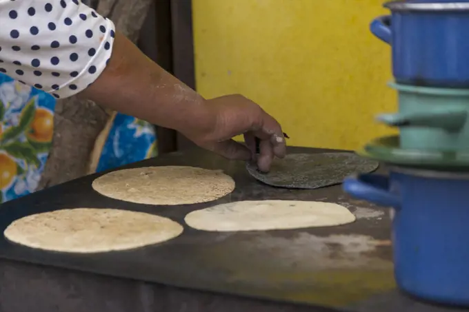 Mexican woman preparing cooking some tortillas on a firewood griddle