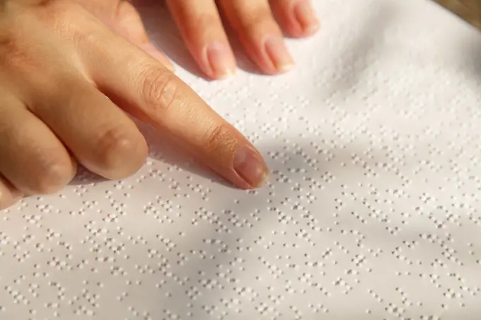 Woman's hand on a book page with braille. Female finger