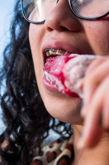 Girl with braces biting a red ice cream in summer