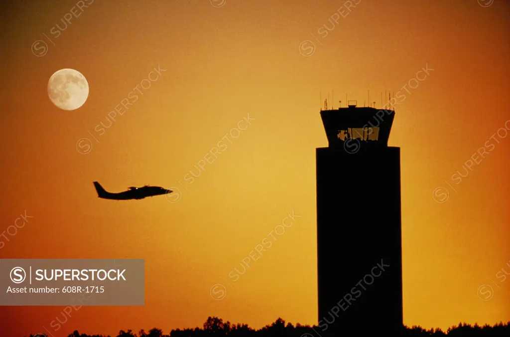 Silhouette of an airplane flying near an air traffic control tower