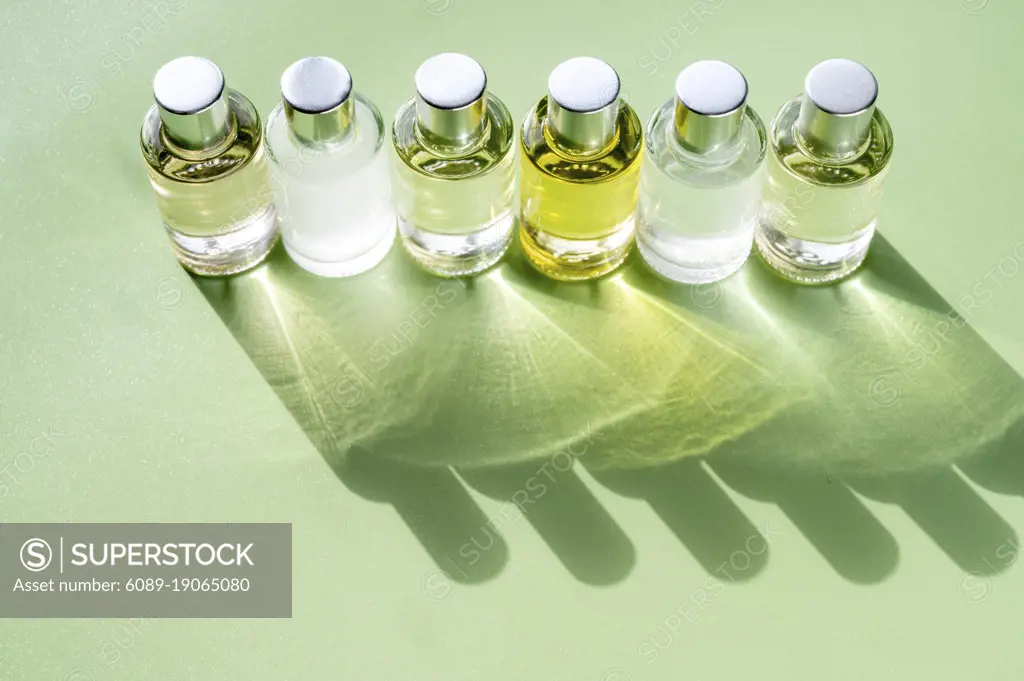 Glass bottle cosmetics with aroma oil for beauty or skin care on green background, natural sun light and shades, top view