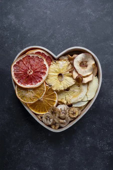Dried fruit slices in heart shaped bowl. Dried orange, grapefruit, pineapples, banana. Healthy snack or desserts