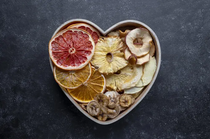 Dried fruit slices in heart shaped bowl. Dried orange, grapefruit, pineapples, banana. Healthy snack or desserts