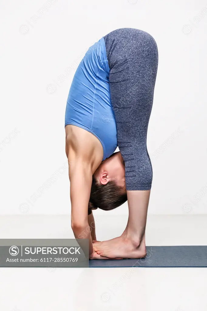 Sporty fit woman practices yoga asana Padahastasana - standing forward bend with hand under feet