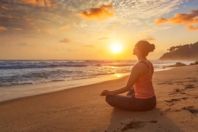 Woman doing yoga - meditate and relax in Padmasana Lotus asana pose with chin mudra outdoors at tropical beach on sunset with dramatic sun