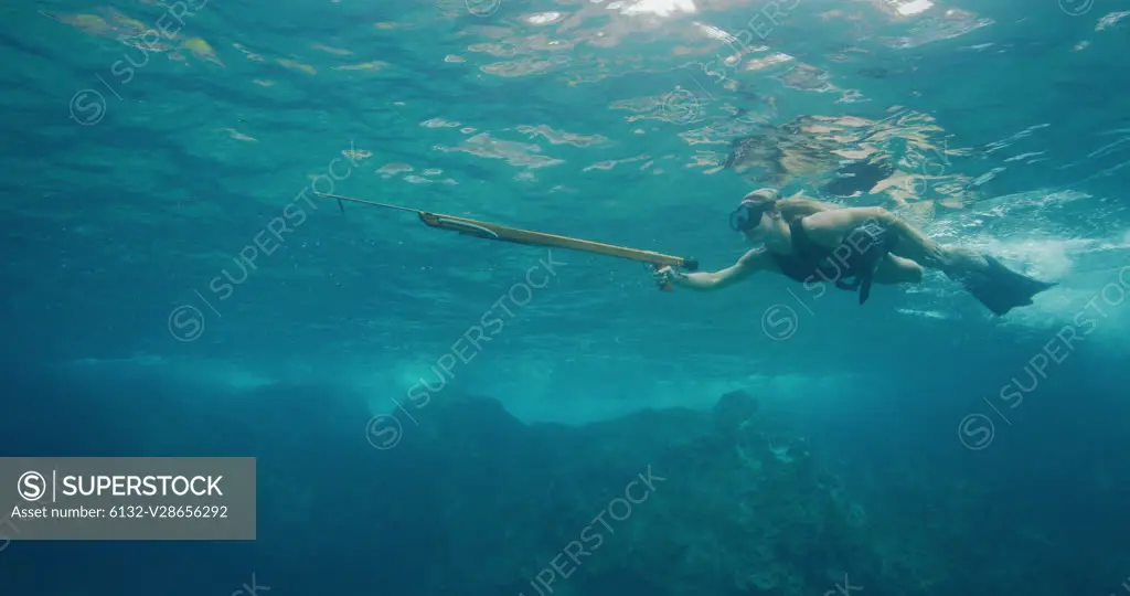 Beautiful freediver woman swimming with her speargun underwater