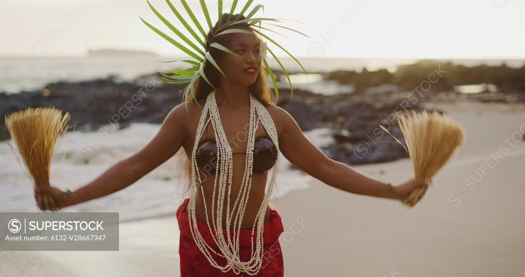 Beautiful polynesian woman performing a Tahitian hula dance on the beach in  slow motion at sunset with the ocean moving in the background - SuperStock