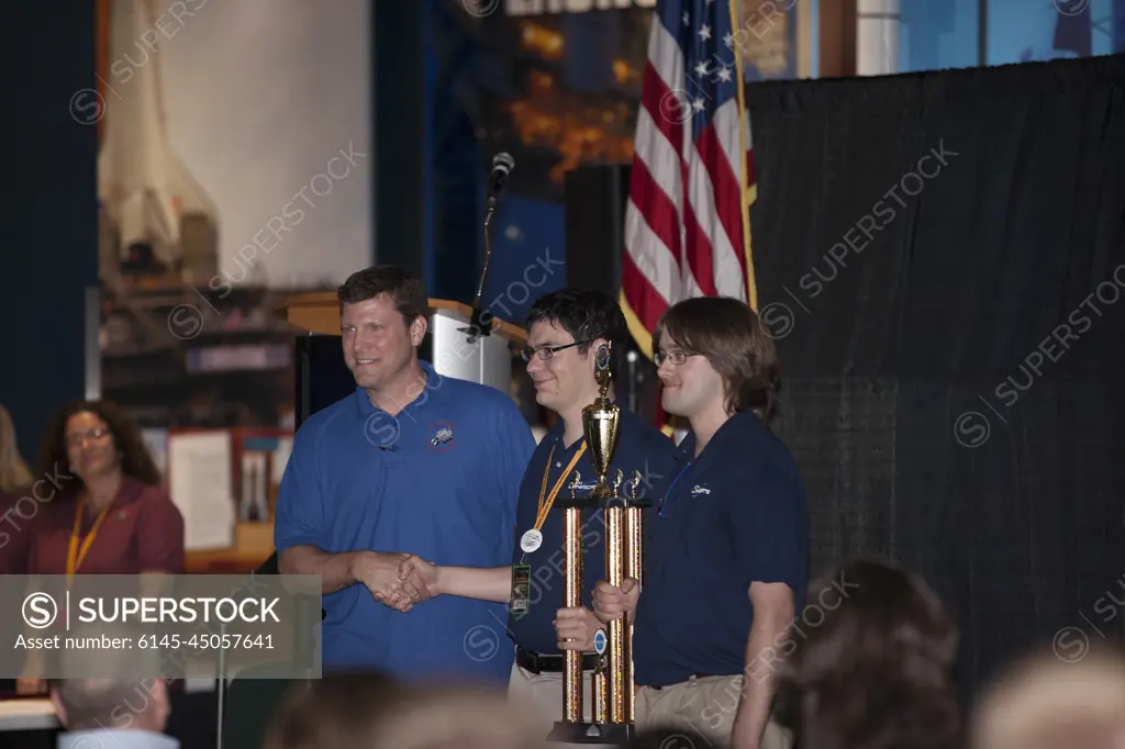 CAPE CANAVERAL, Fla. -- Kennedy Space Center engineer Marc Seibert presents the Communication Award to the University of New Hampshire team members during NASA's 2014 Robotic Mining Competition award ceremony inside the Space Shuttle Atlantis attraction at the Kennedy Space Center Visitor Complex in Florida. The team moved 10 kilograms of simulated Martian soil with its robot while using the least amount of communication power. More than 35 teams from colleges and universities around the U.S. designed and built remote-controlled robots for the mining competition. The competition is a NASA Human Exploration and Operations Mission Directorate project designed to engage and retain students in science, technology, engineering and mathematics, or STEM, fields by expanding opportunities for student research and design. Teams use their remote-controlled robotics to maneuver and dig in a supersized sandbox filled with a crushed material that has characteristics similar to Martian soil. The o