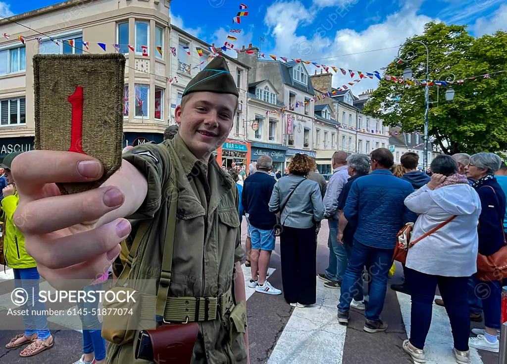 A kid from Carentan holds up a 1st Infantry Division patch during a D-Day commemoration parade at Carentan, France, June 6, 2022. This year, U.S. Army Europe and Africa commemorates the 78th anniversary of D-Day, the largest multi-national amphibious landing and operational military airdrop in history, and highlights the U.S.' steadfast commitment to European allies and partners.
