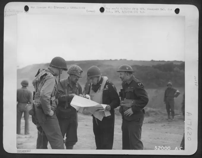 Officers of one of Bulldozer battalions of the Ninth Engineer Command which built the first American emergency landing strip on the Continent pause on one of the beach-heads on "D-Day" plus one to examine a map with Maj. Gen. Ralph Royce, deputy