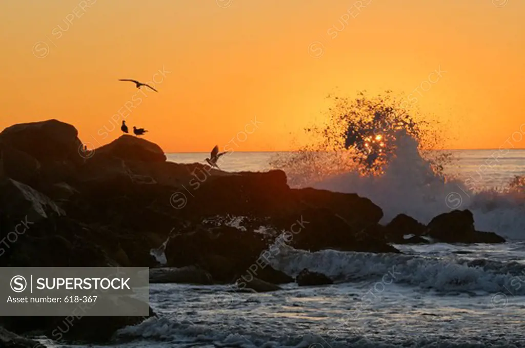 USA, California, Los Angeles, Westchester, Dockweiler Beach, Waves crashing against rocks at sunset