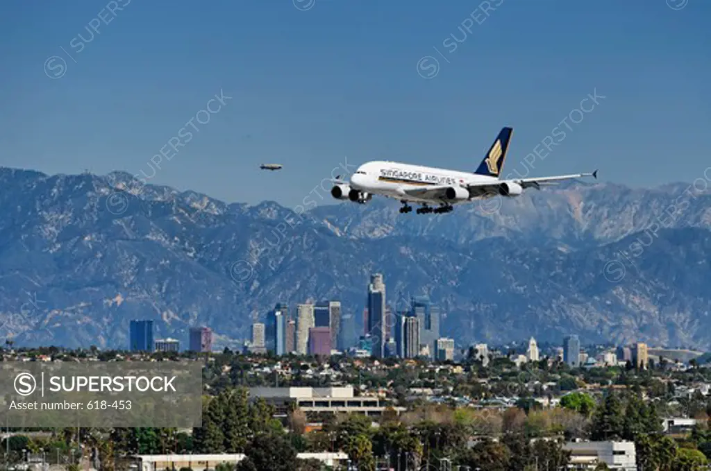 USA, California, Los Angeles, Singapore Airlines operated Airbus A380-841 super jumbo approaching Los Angeles International Airport, LAX, Westchester, In background downtown Los Angeles office towers and San Gabriel Mountains, In distance Good Year blimp