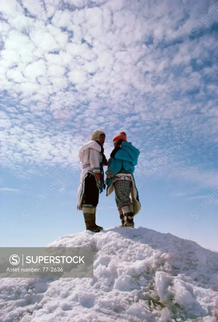 Two Eskimos standing on a snow covered hill, Arctic