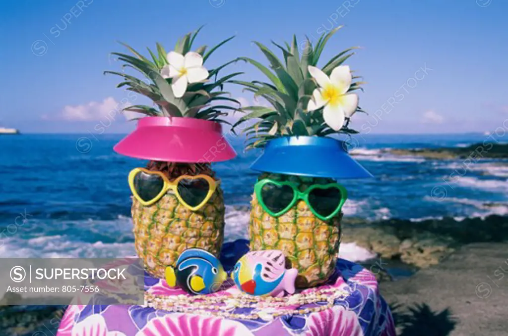 Close-up of two pineapples with heart shaped sunglasses and sun visors