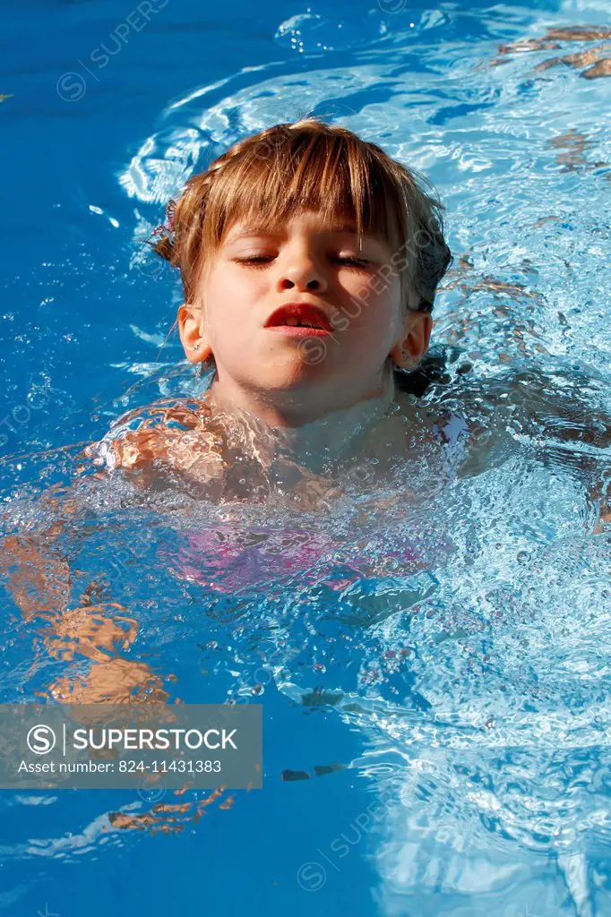 A 6-year old girl swimming for the first time without armbands in a swimming pool.