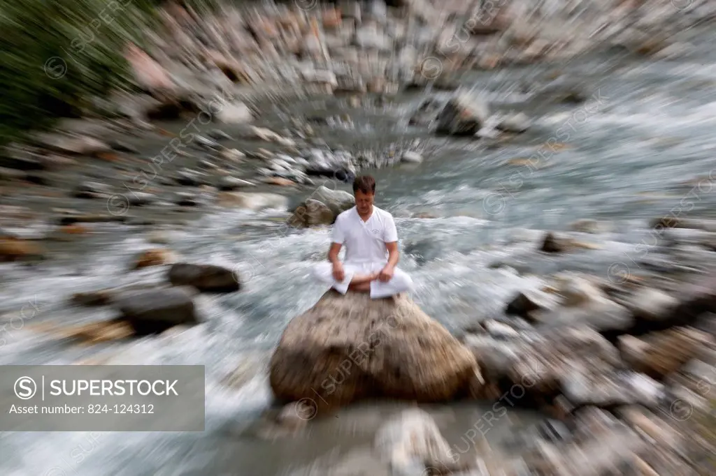 Man meditating in the lotus position, sitting on a rock by the river.
