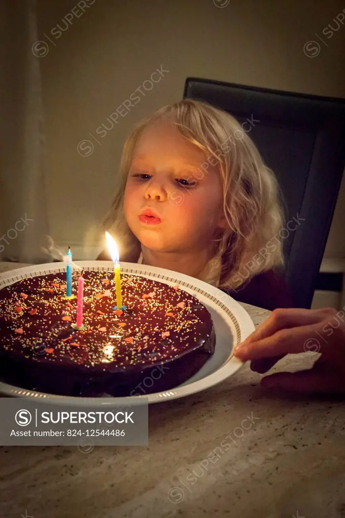 Three-year-old girl blowing out candles on birthday cake.
