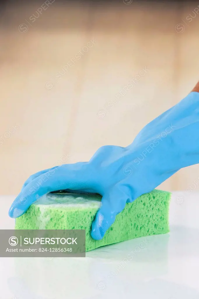 Woman wearing rubber gloves using washing sponge.
