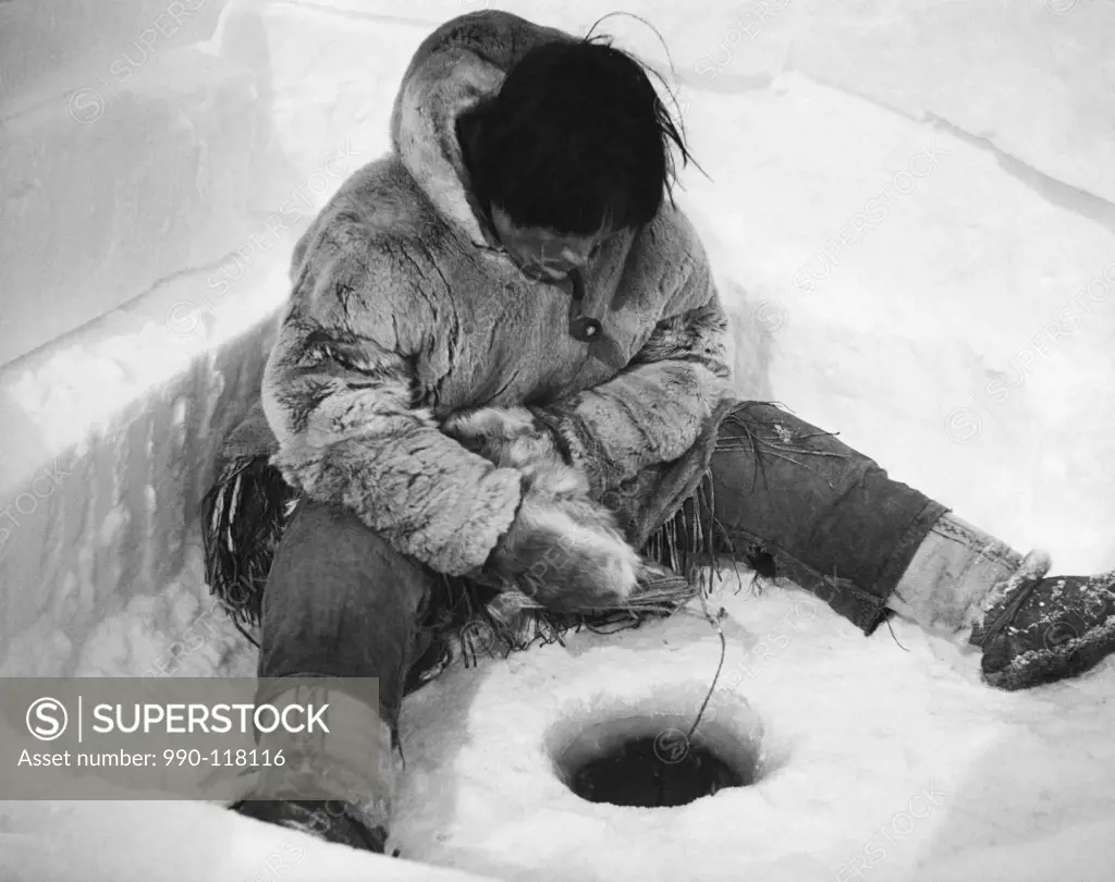 Eskimo fisherman sitting near a hole and fishing, Alaska, USA