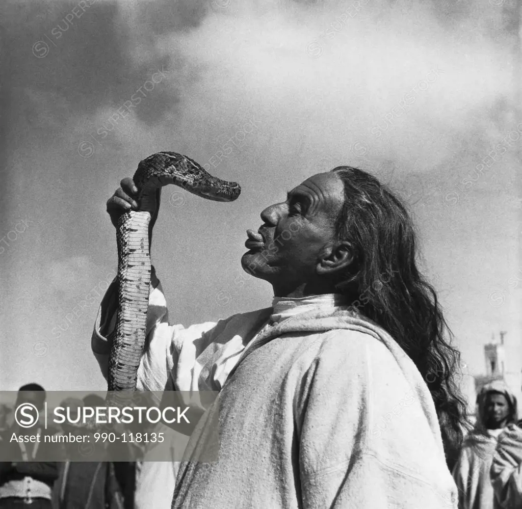 Snake charmer sticking his tongue out and holding a snake, Marrakesh, Morocco