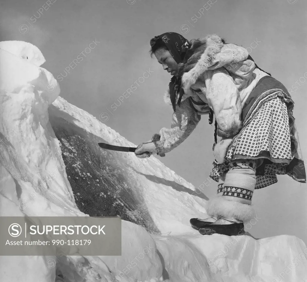 Low angle view of an Eskimo woman scraping frost from an igloo window