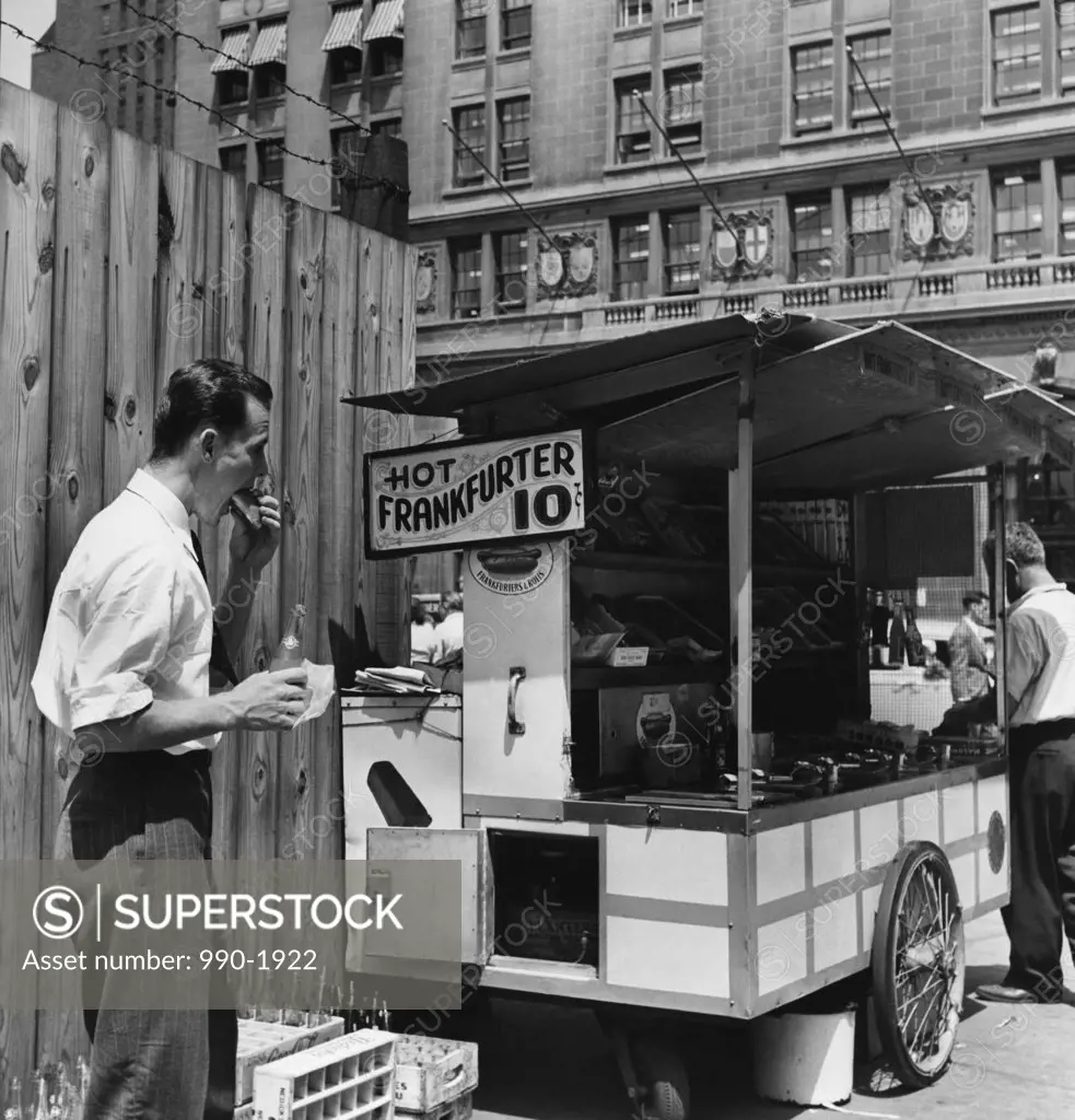 Mid adult man eating food near a hot dog stand, New York City, New York, USA