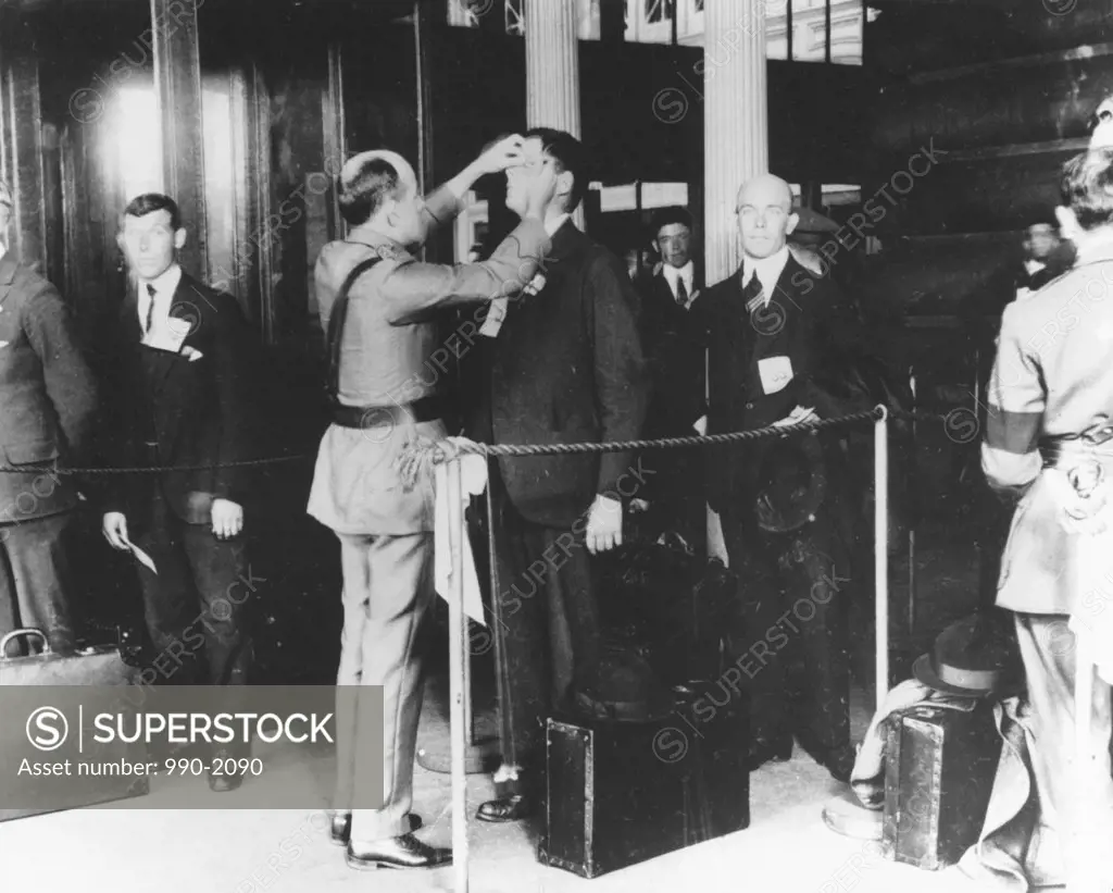 Rear view of a police officer examining a man in an immigration office, Ellis Island, New York City, New York, USA