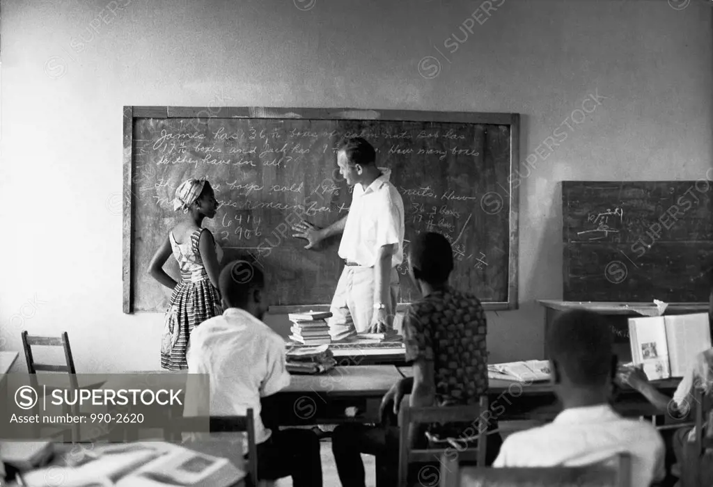 Side profile of a teacher teaching a girl standing near a blackboard, Bopolu, Liberia