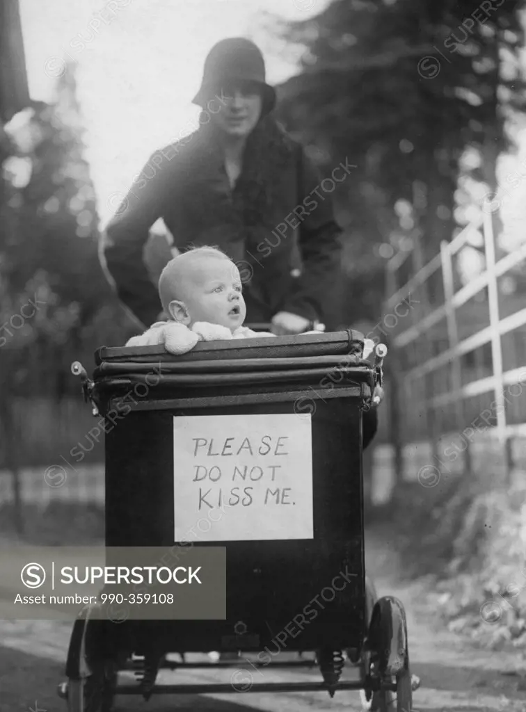 Mother with baby in baby stroller with 'please do not kiss me' placard