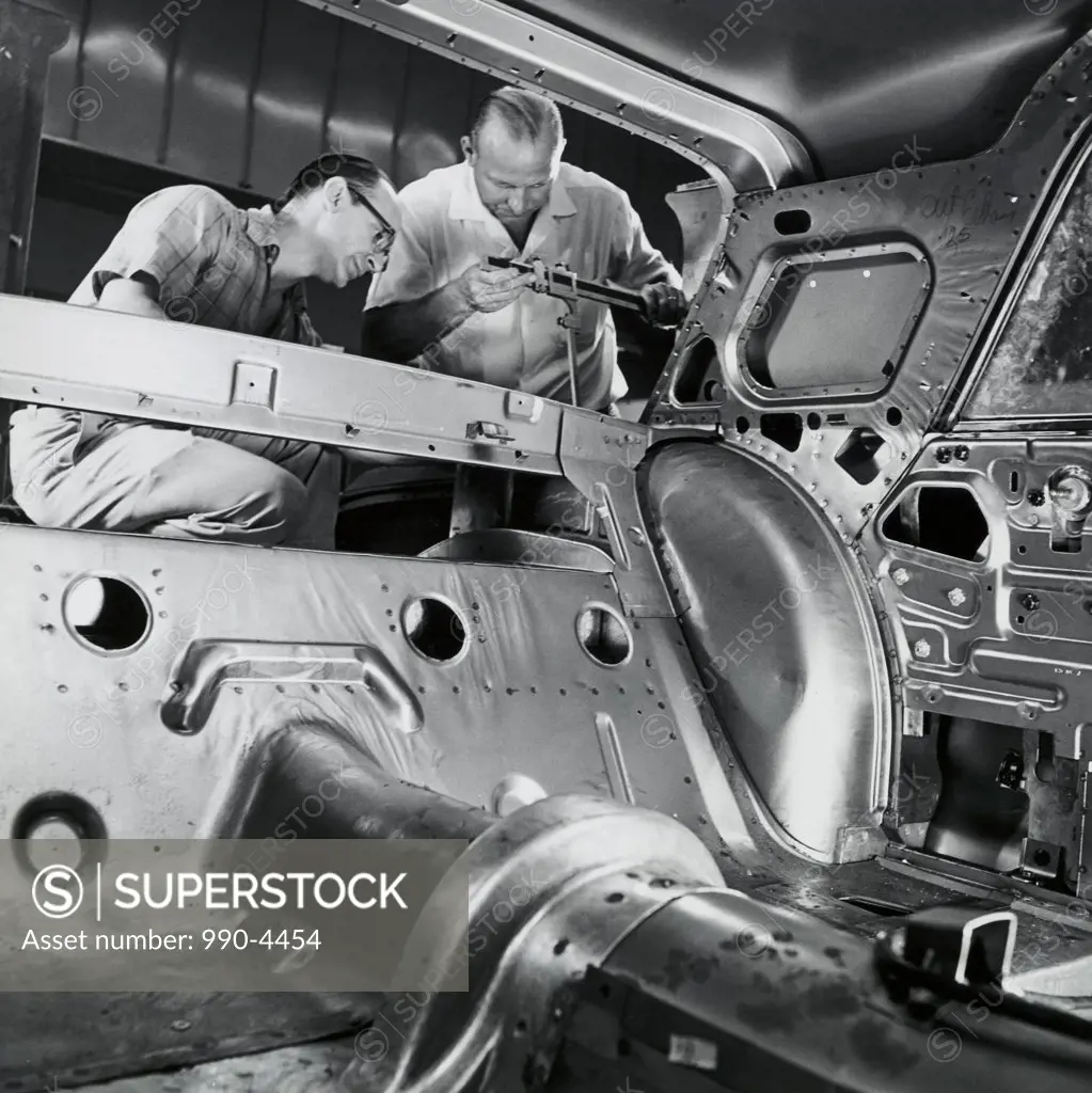 Low angle view of two male workers working in a car assembly plant