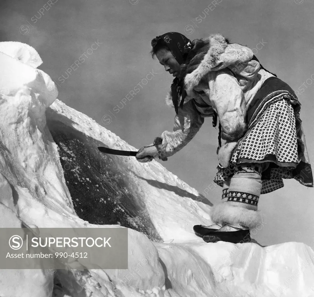 Low angle view of an Eskimo woman cutting ice with a knife, Alaska, USA
