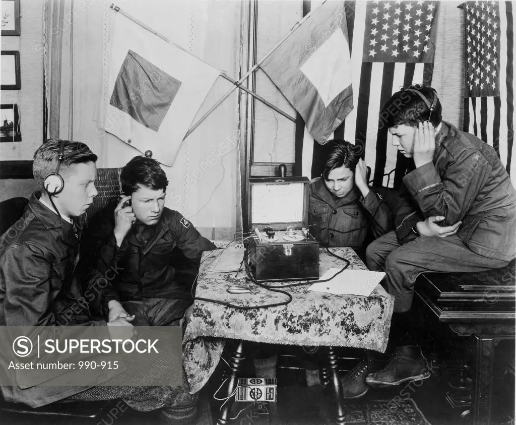 Four teenage boys listening to a radio using headphones